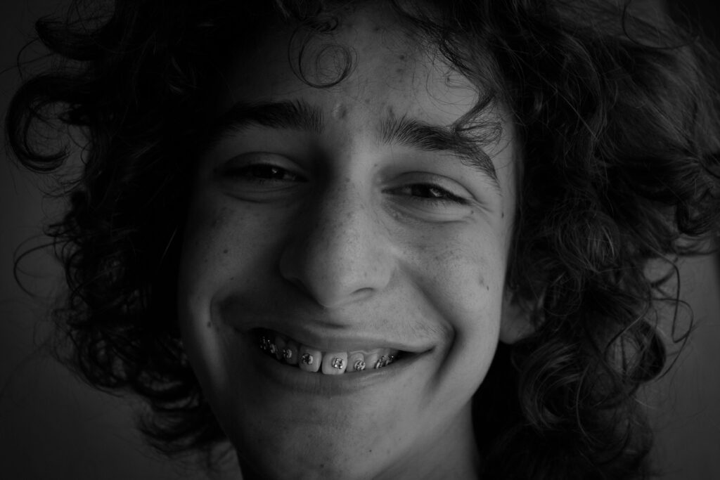 Close-up black and white portrait of a smiling teenager with curly hair and braces, exuding happiness.